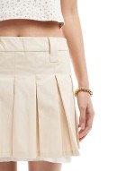 pleated mini skirt with white layered raw hem detail in beige